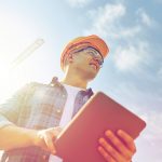 construction worker with sun, blue sky and a big crane in the background