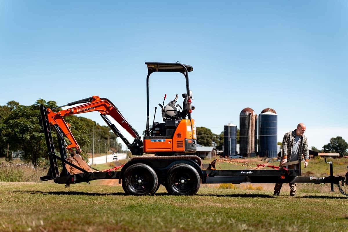 open trailer with a Hitachi mini excavator on trailer man is loading